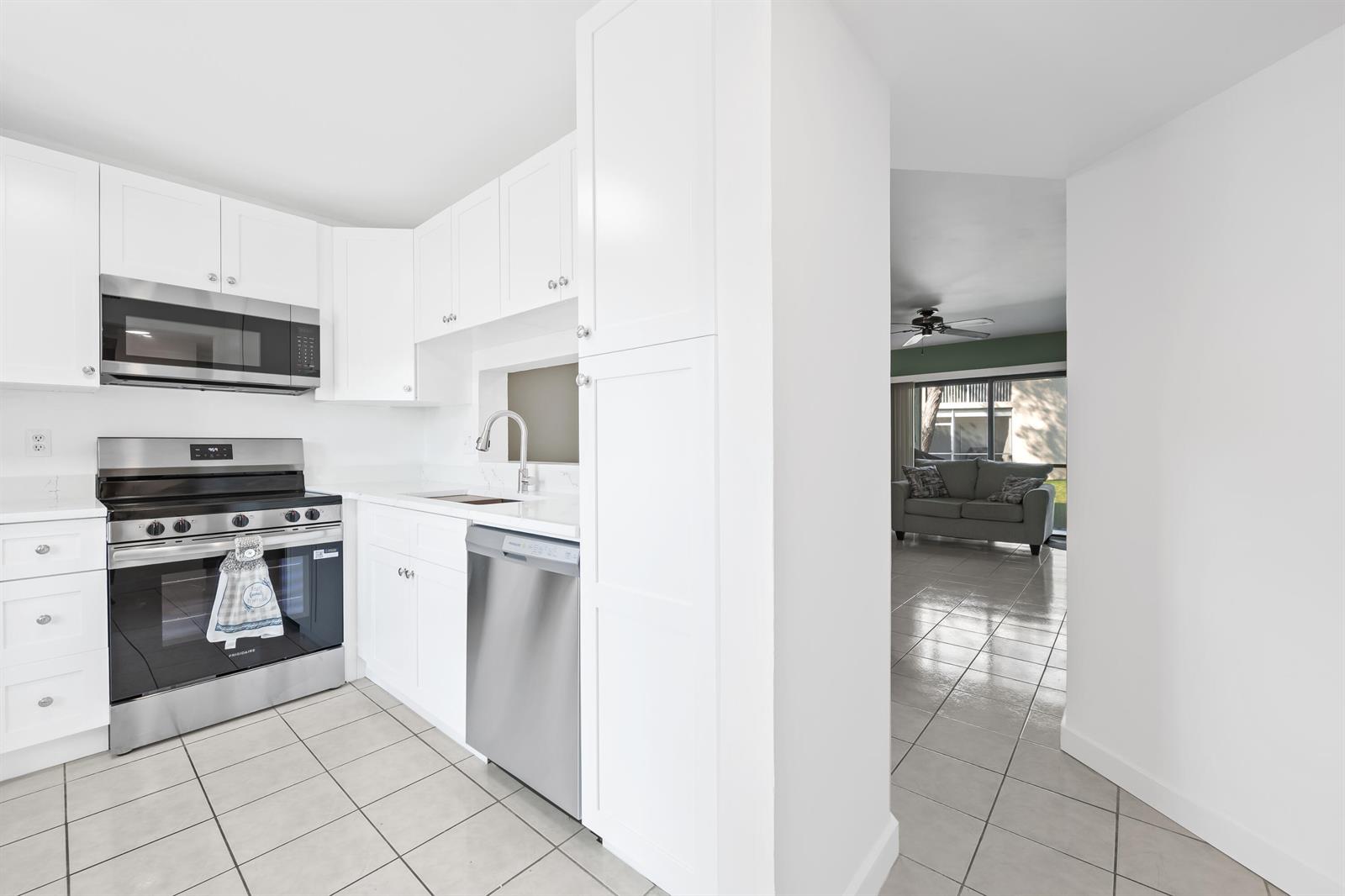 A white kitchen with stainless steel appliances opens into a living area with tiled floors — 5570 Lakeside Drive # 102, Margate FL 33063, MARGATE, FL
