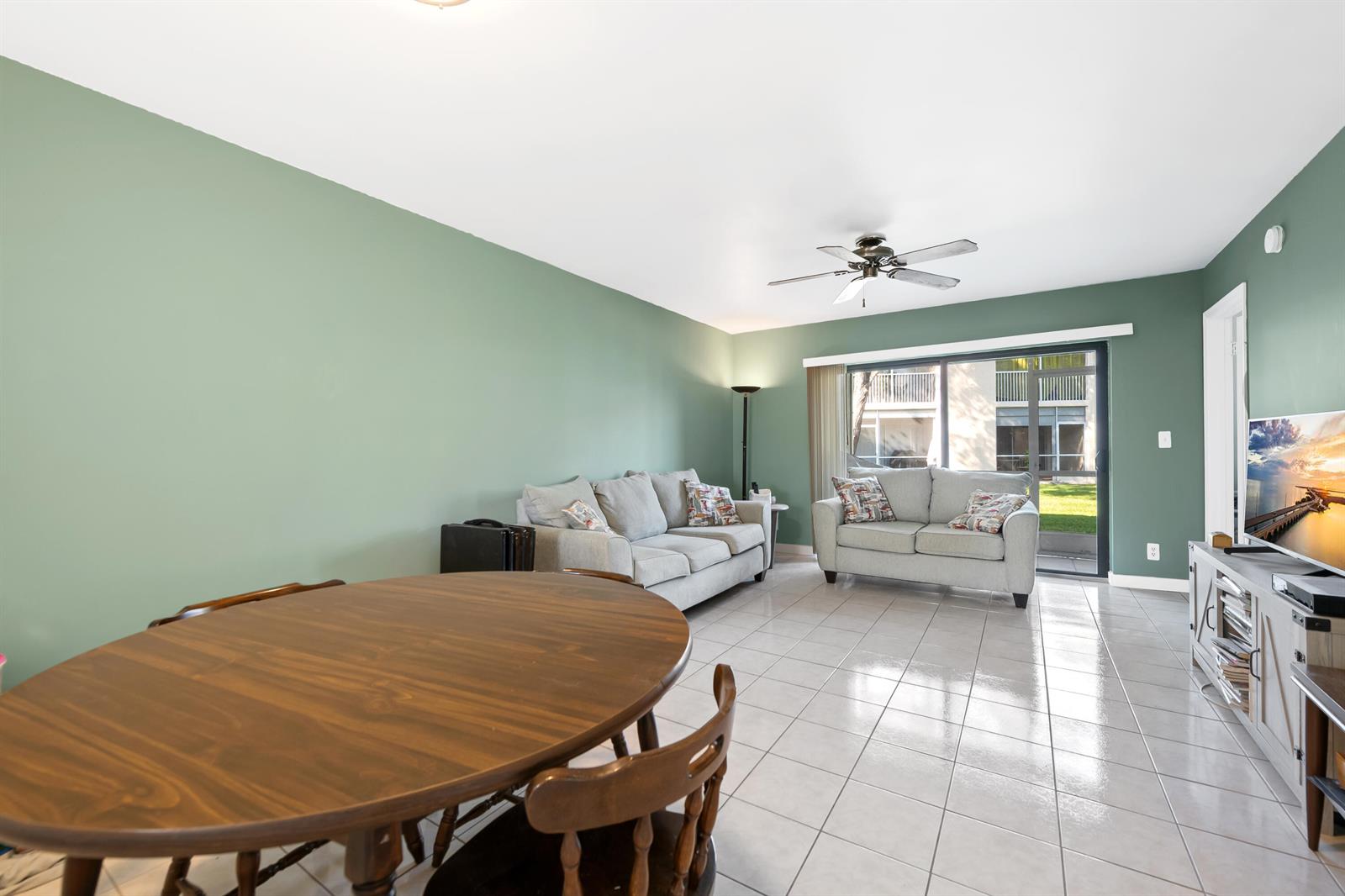 A living and dining area features sage green walls, tile flooring, and a sliding glass door — 5570 Lakeside Drive # 102, Margate FL 33063, MARGATE, FL