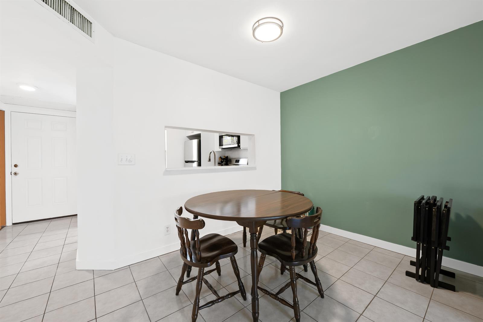 A dining area features a round wooden table, four chairs, and a green accent wall — 5570 Lakeside Drive # 102, Margate FL 33063, MARGATE, FL
