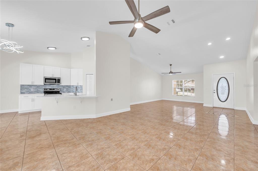 An open-concept kitchen and living area features white cabinetry, tile flooring, and ceiling fans — 2910 LOTUS CT, KISSIMMEE, FL