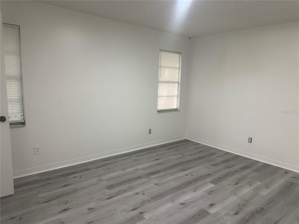 An empty bedroom features white walls, two windows with blinds, and gray wood-look flooring — 8426 CAMDEN STREET UNIT D, TAMPA, FL