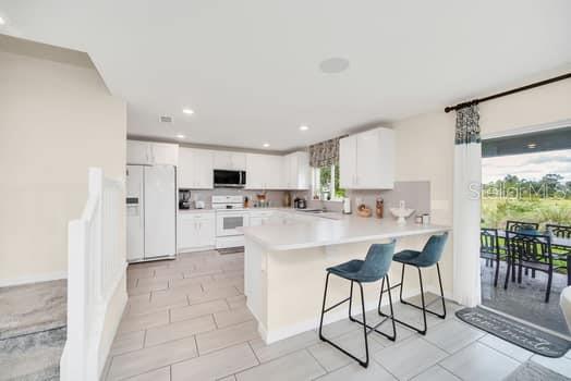 A kitchen with white cabinets, a breakfast bar with two stools, and a sliding glass door — 321 PRESERVE POINTE BOULEVARD, DAVENPORT, FL