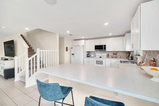 A kitchen with white cabinets and a breakfast bar overlooks a staircase with white railings — 321 PRESERVE POINTE BOULEVARD, DAVENPORT, FL