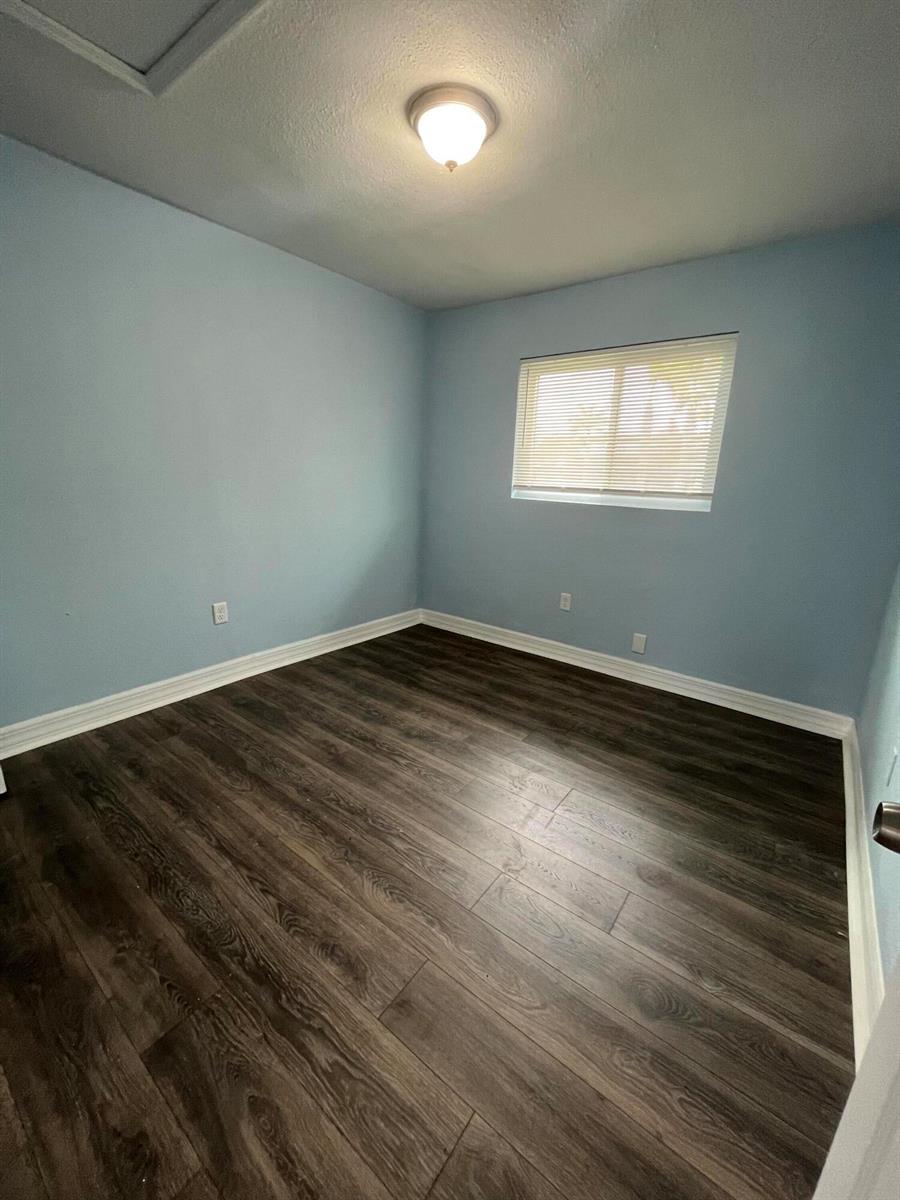 An empty bedroom with light blue walls, dark wood-look flooring, and a single window — 1109 NW 6th Avenue Apt 1, Pompano Beach FL 33060, POMPANO BEACH, FL