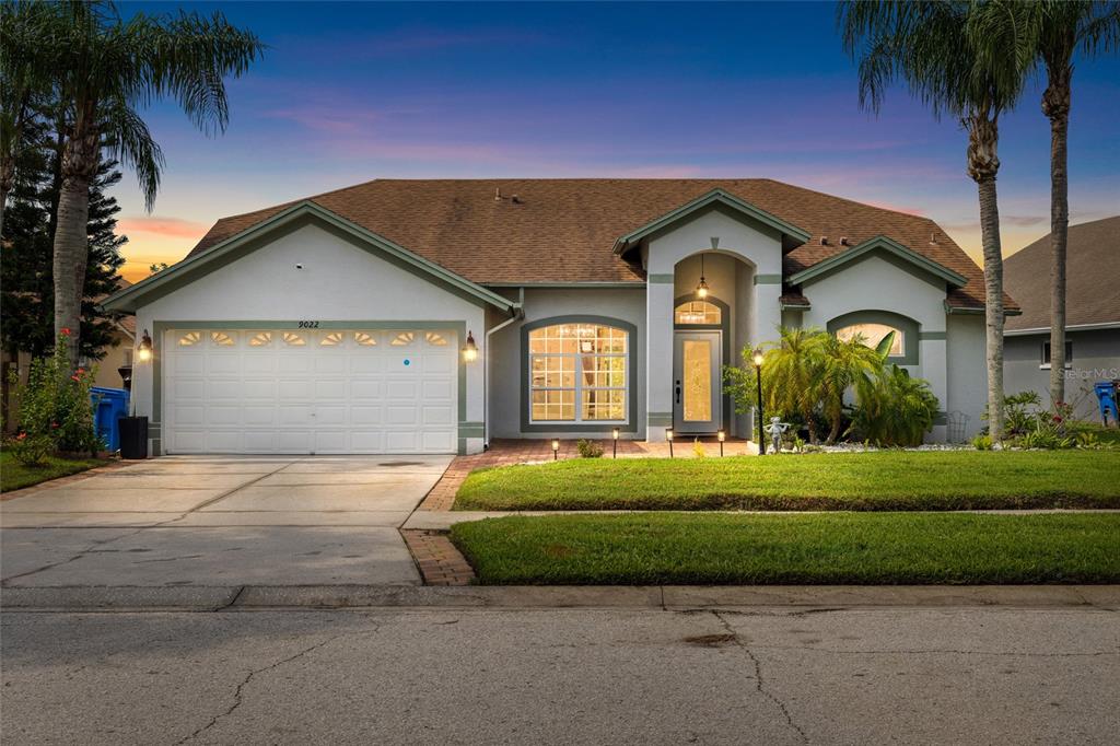 A single-story suburban house with a white stucco facade, a two-car garage, and palm trees — 9022 WESTBAY BOULEVARD, TAMPA, FL