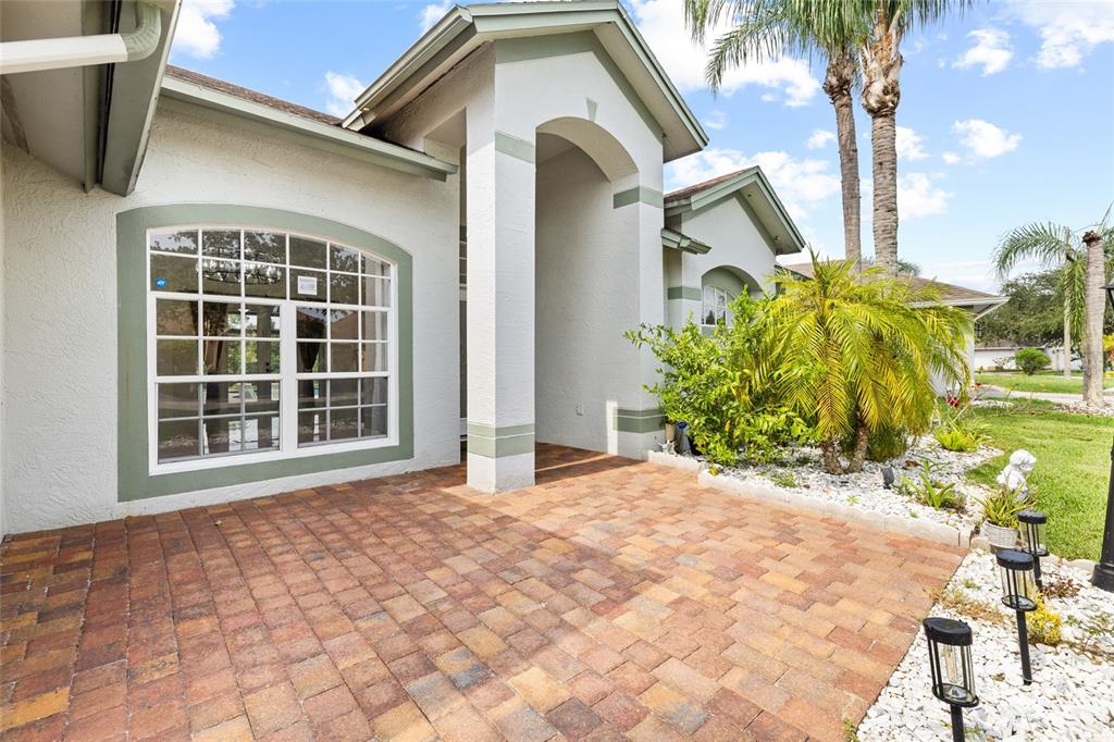 A paved front patio leads to the arched entryway of a light-colored stucco house — 9022 WESTBAY BOULEVARD, TAMPA, FL