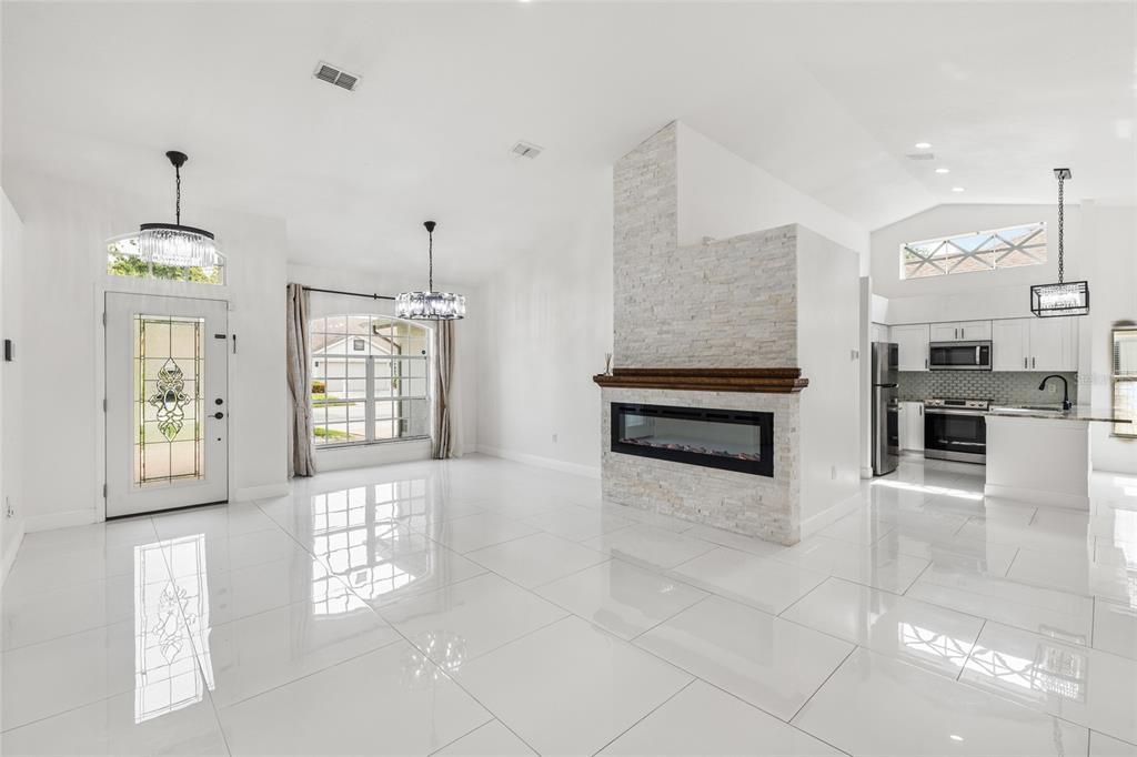 A bright living room features white tile floors, a stone fireplace, and an open kitchen — 9022 WESTBAY BOULEVARD, TAMPA, FL