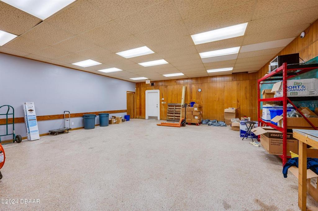 A large, empty storage room features wood-paneled walls, a drop ceiling, and concrete flooring — 116 CENTER STREET, DAYTONA BEACH, FL