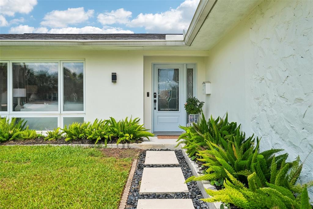 A light-colored house exterior features a glass-paneled front door, stone wall, and fern landscaping — 4379 44TH STREET S, ST PETERSBURG, FL