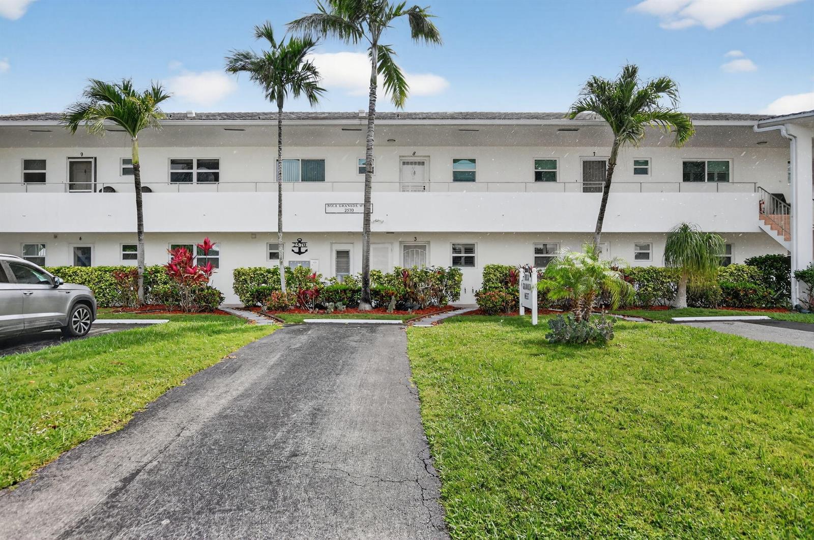 A two-story white apartment building features palm trees, a paved driveway, and landscaped shrubbery — 2570 Banyan Road Unit 3, Boca Raton FL 33432, BOCA RATON, FL