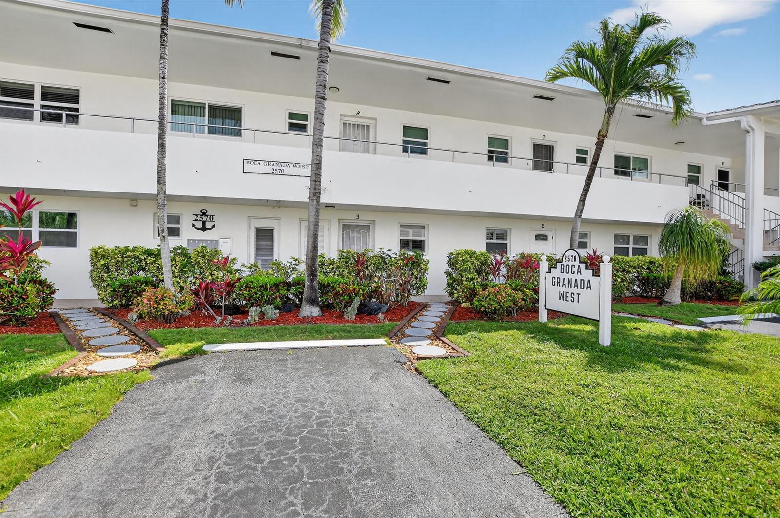 A two-story white apartment building features a paved walkway, landscaping, and a prominent sign — 2570 Banyan Road Unit 3, Boca Raton FL 33432, BOCA RATON, FL