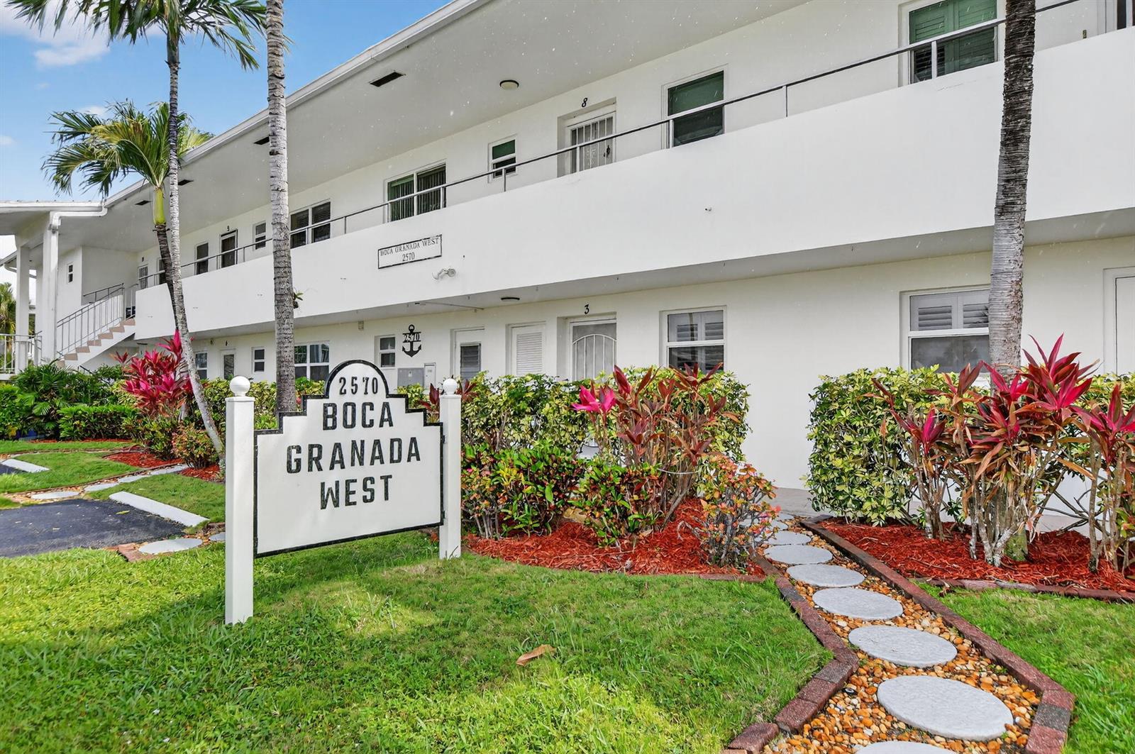 The exterior of a two-story white apartment building with a prominent signage board in front — 2570 Banyan Road Unit 3, Boca Raton FL 33432, BOCA RATON, FL