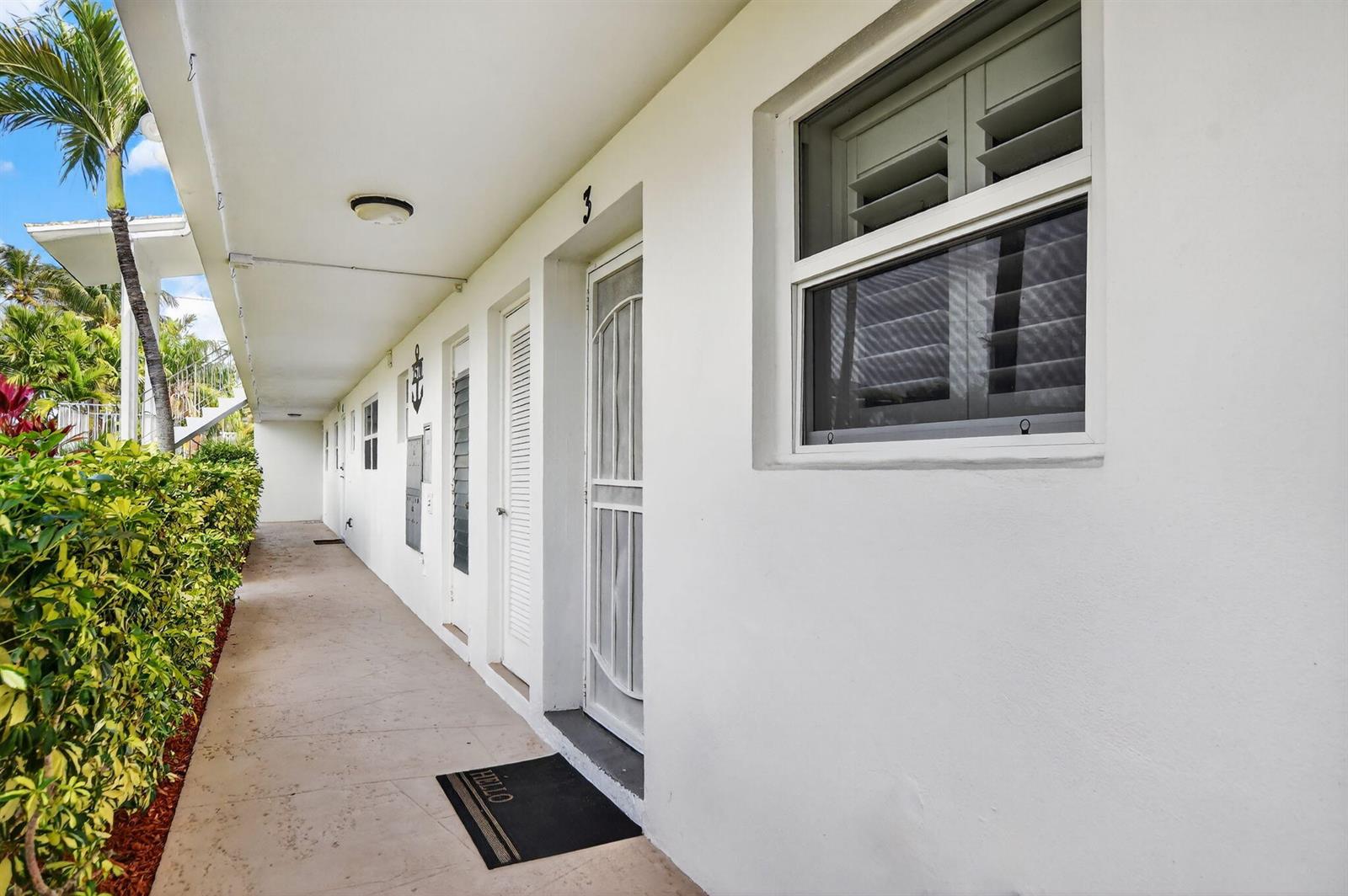 An exterior walkway leads past white doors and windows of a multi-unit residential building — 2570 Banyan Road Unit 3, Boca Raton FL 33432, BOCA RATON, FL