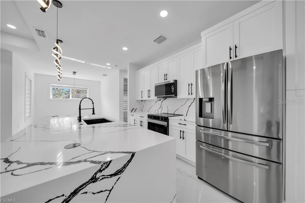 A modern kitchen features white marble countertops with black veining, white cabinetry, and stainless appliances — 7799 15TH PL, LABELLE, FL