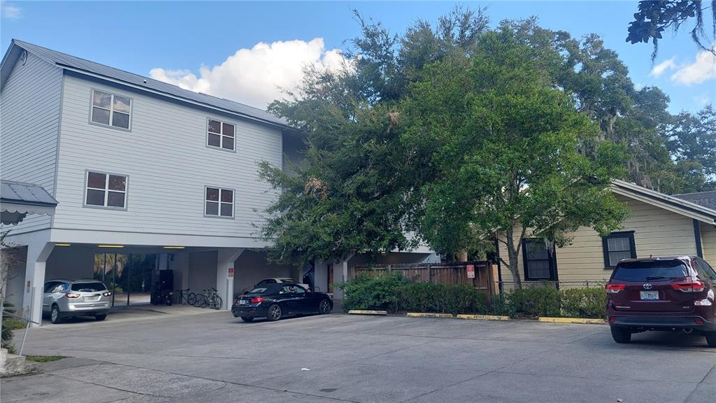 A multi-story building with covered parking sits next to a smaller house and parking lot — 1615 NW 3RD AVENUE, GAINESVILLE, FL