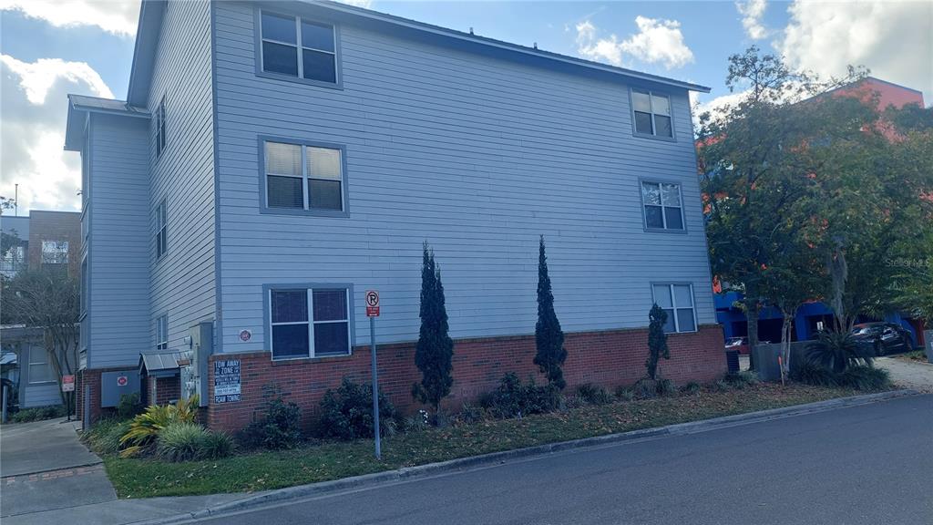 A three-story building with light blue siding and a brick base sits beside a road — 1615 NW 3RD AVENUE, GAINESVILLE, FL