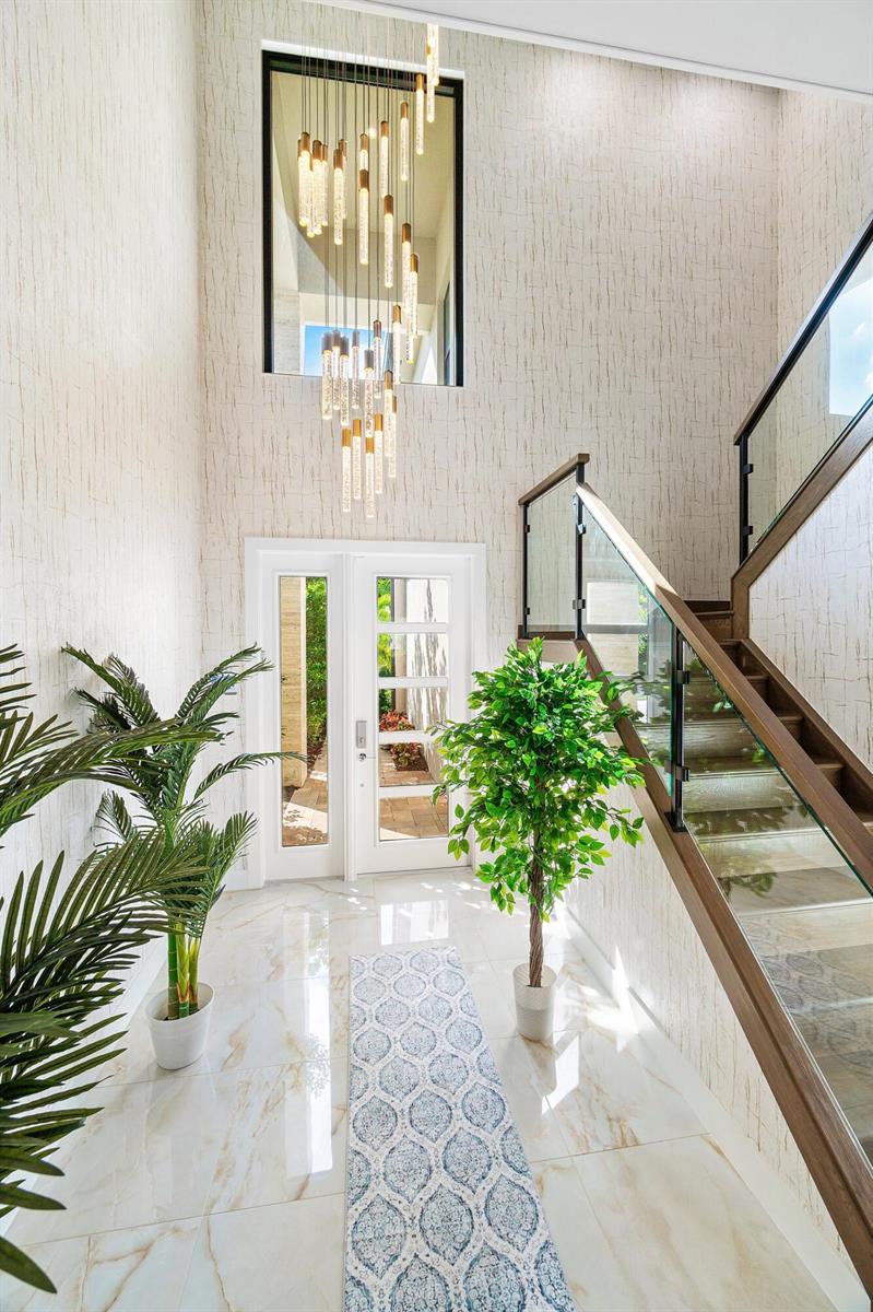 A bright entryway features a tall chandelier, marble floors, a staircase, and two potted plants — 8233 Crystal Downs Avenue, Boca Raton FL 33434, BOCA RATON, FL