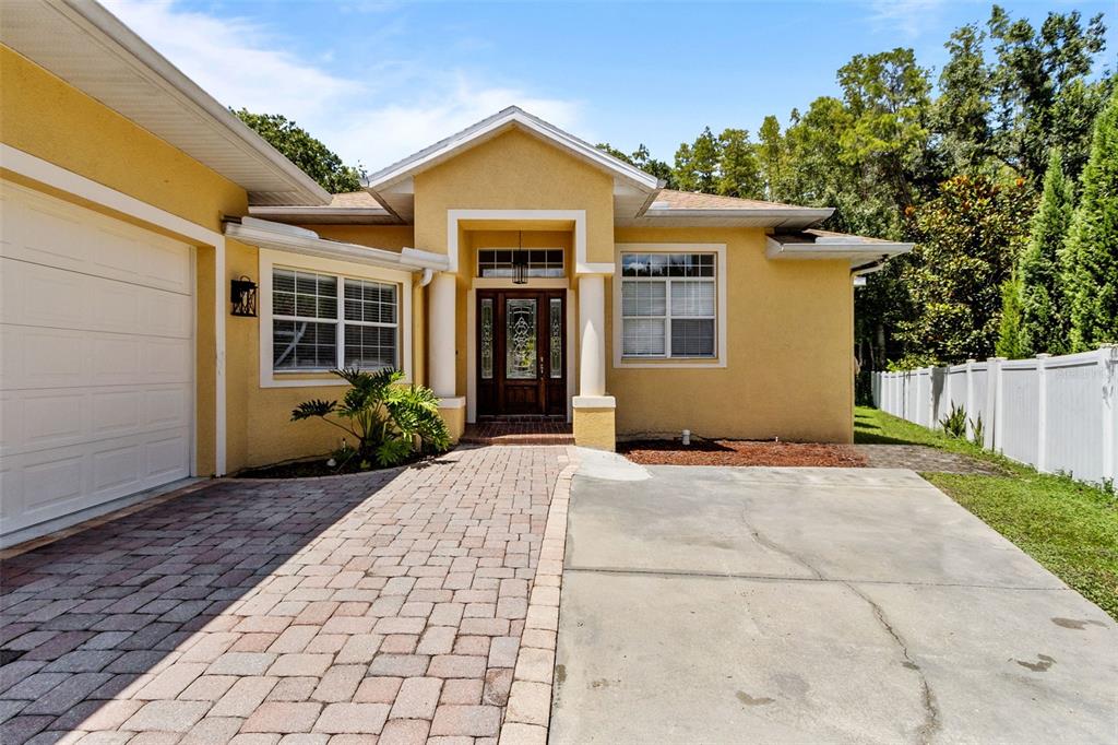A yellow stucco house features a paver walkway, a concrete driveway, and a front entrance — 4116 WOODACRE LANE, TAMPA, FL