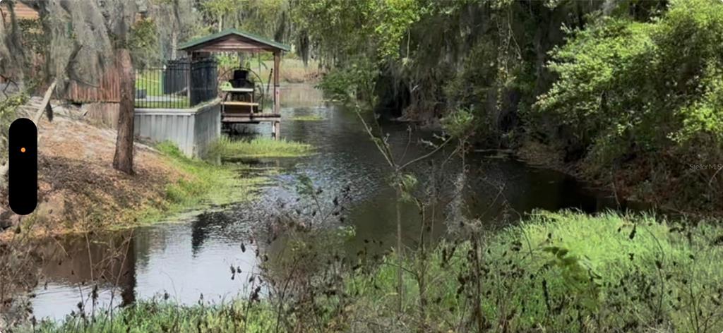 A small wooden dock with a roof sits along a narrow canal lined with trees — CEDAR CIR, LAKE WALES, FL