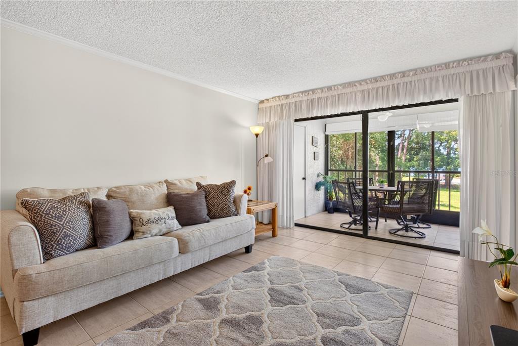 A living room with a beige sofa, tile flooring, and a sliding door to a balcony — 3276 CANDLE RIDGE COURT UNIT 202, ORLANDO, FL