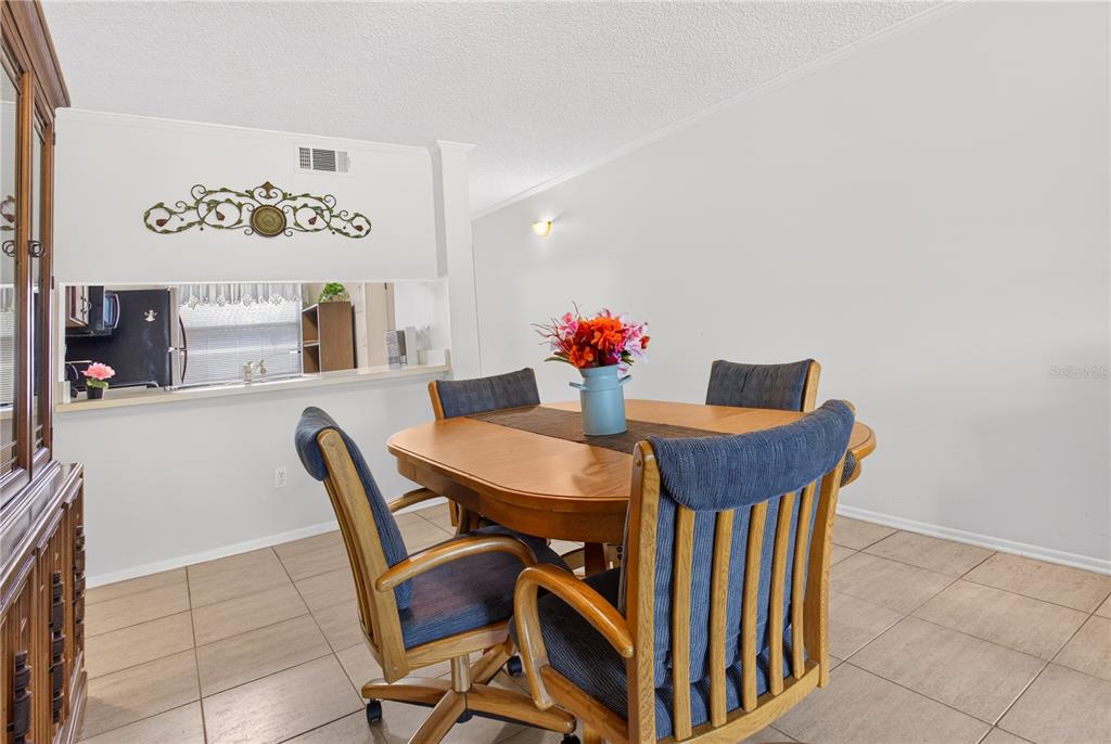 A dining area features a wooden table with four blue chairs on tiled flooring — 3276 CANDLE RIDGE COURT UNIT 202, ORLANDO, FL