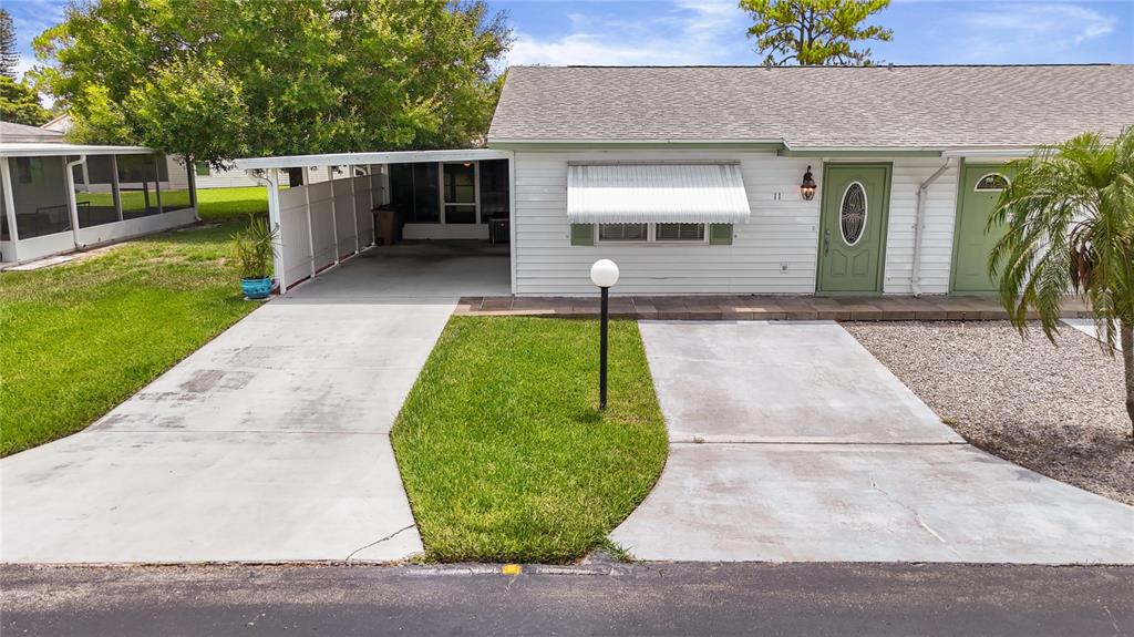 A single-story house with a carport, a green front door, and a concrete driveway — 11 DESERT CANDLE CIRCLE, LEHIGH ACRES, FL