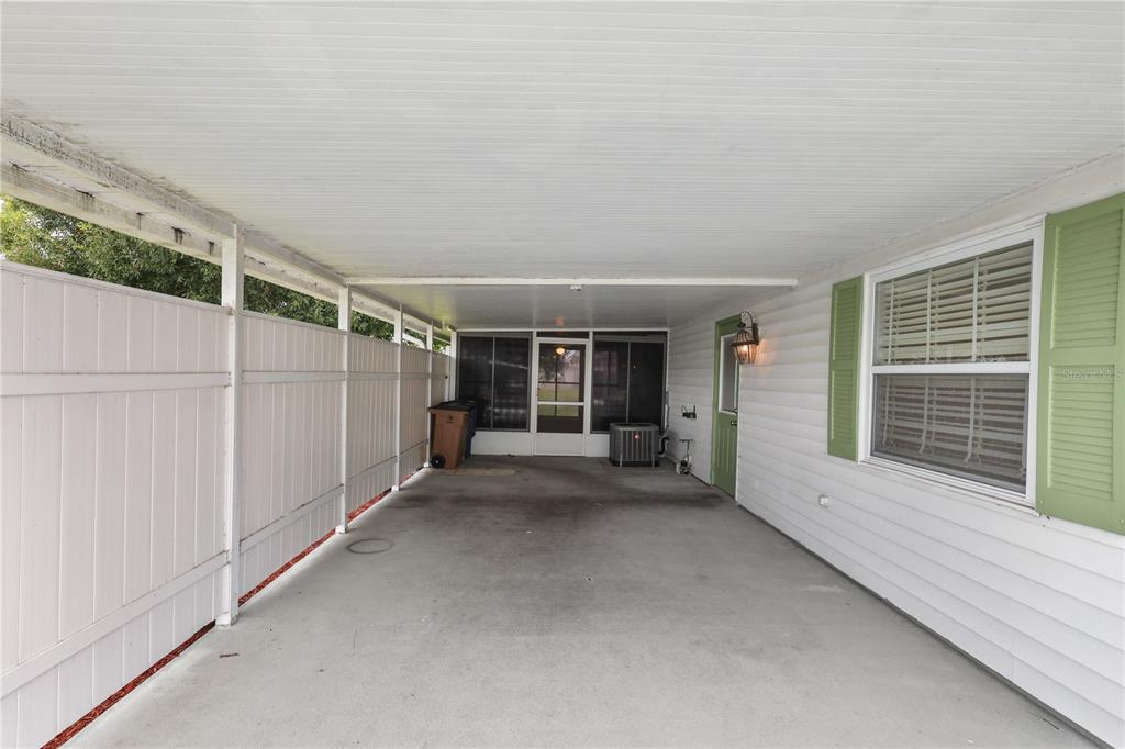 A covered carport with a concrete floor, white vinyl fencing, and a green door — 11 DESERT CANDLE CIRCLE, LEHIGH ACRES, FL