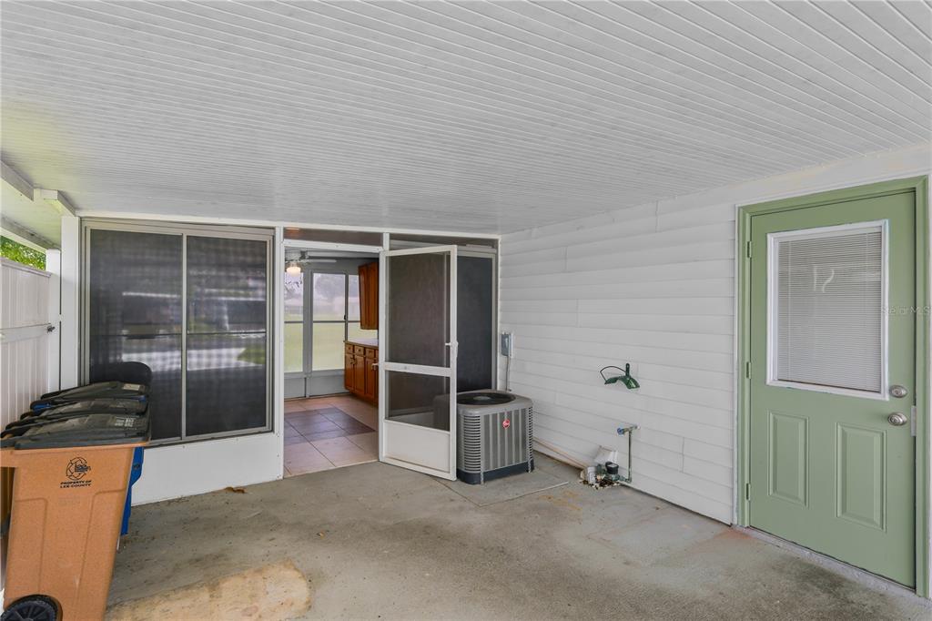 A covered concrete patio features a green door, an outdoor AC unit, and a screened entrance — 11 DESERT CANDLE CIRCLE, LEHIGH ACRES, FL
