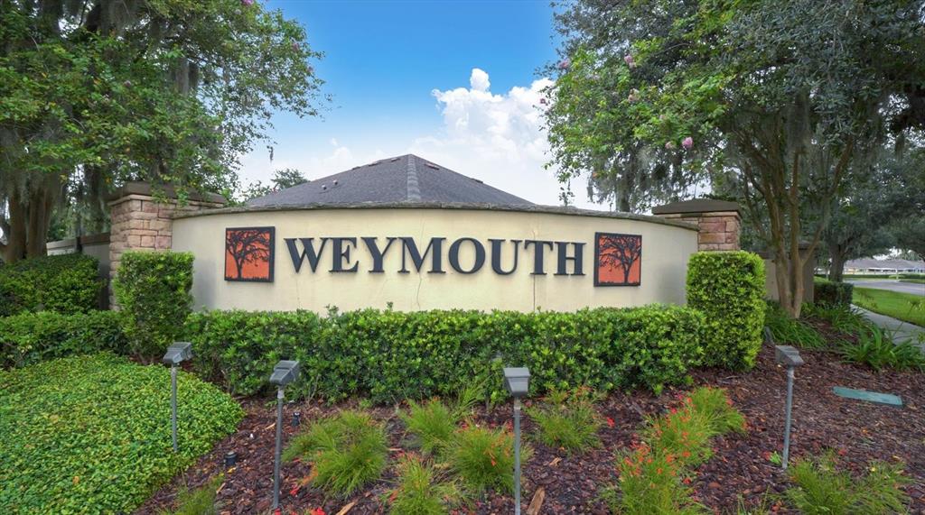 A curved stone monument sign displays the name Weymouth in a landscaped residential entrance area — 19320 HASKELL PLACE, LAND O LAKES, FL
