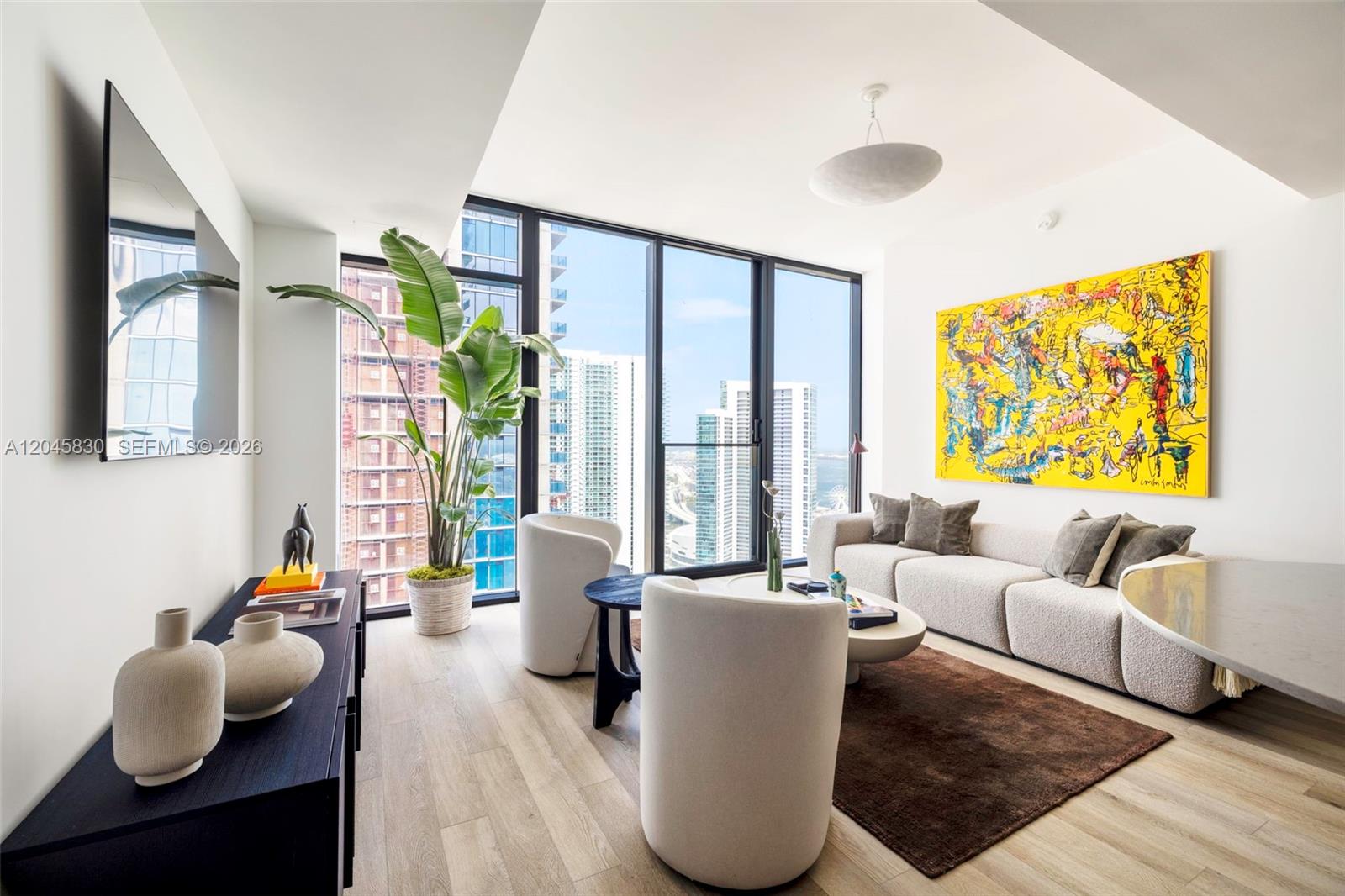 A modern living room features a yellow abstract painting, white curved chairs, and floor-to-ceiling windows — 20 NE 11th St # 4503, Miami FL 33132, MIAMI, FL