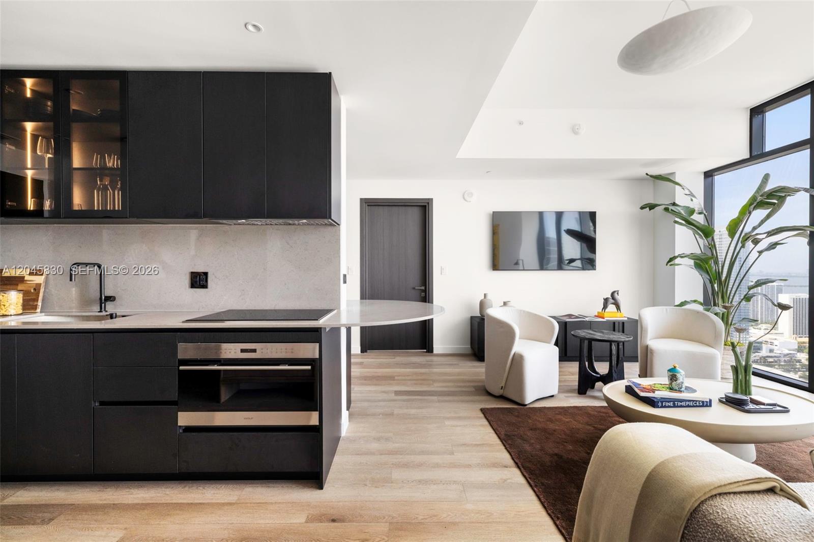 A modern kitchen with dark cabinetry and a living area with floor-to-ceiling windows — 20 NE 11th St # 4503, Miami FL 33132, MIAMI, FL