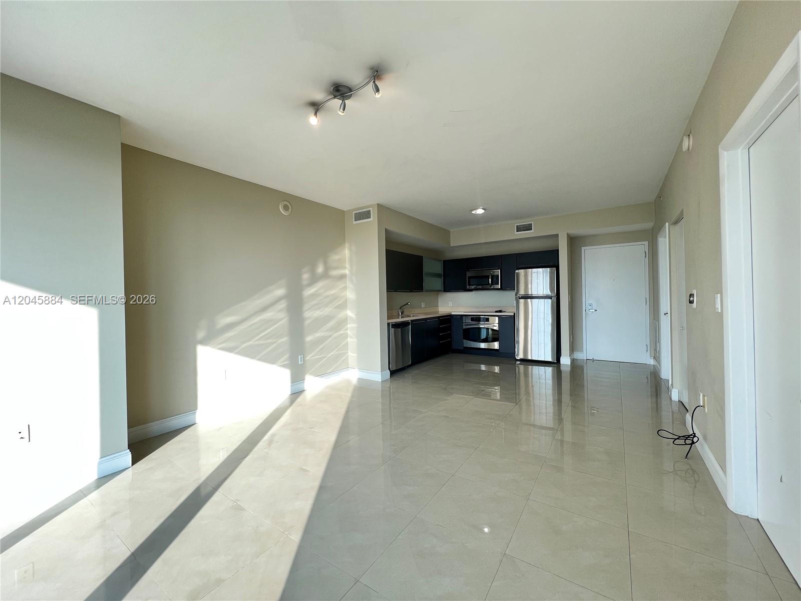 An open-concept kitchen with dark cabinetry and stainless steel appliances overlooks a tiled living area — 90 SW 3rd St # 1710, Miami FL 33130, MIAMI, FL