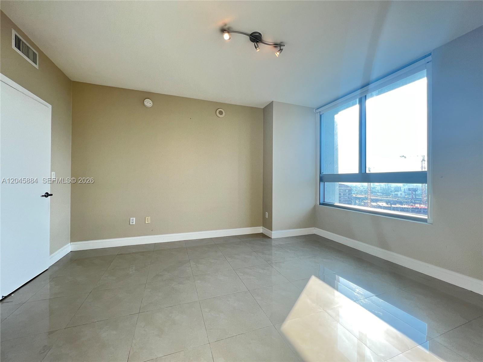 An empty room features beige walls, large floor tiles, a track light, and a window — 90 SW 3rd St # 1710, Miami FL 33130, MIAMI, FL