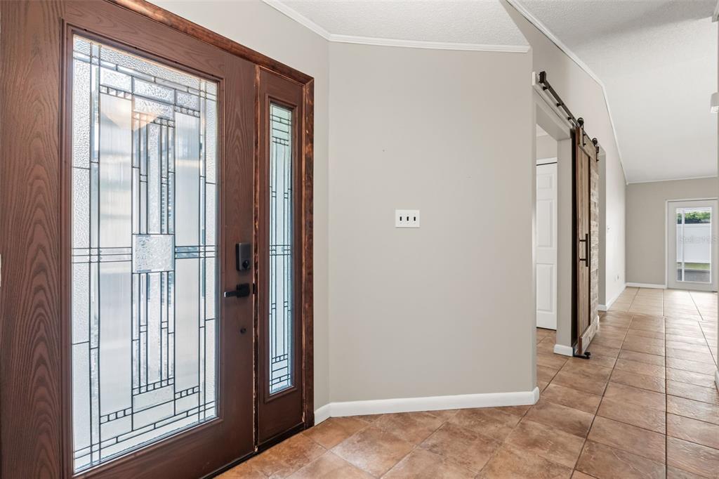 A foyer with tile flooring, a decorative glass front door, and a sliding barn door — 1275 BRIDLEBROOK DRIVE, CASSELBERRY, FL