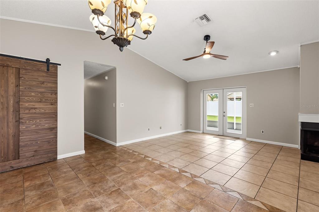A living room features tile flooring, a vaulted ceiling, a ceiling fan, and a barn door — 1275 BRIDLEBROOK DRIVE, CASSELBERRY, FL