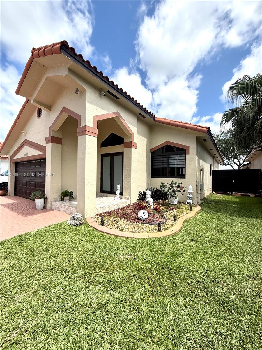 A single-story house with a tan stucco exterior, a tiled roof, and a front garden — 8731 NW 153rd Ter, Miami Lakes FL 33018, MIAMI LAKES, FL