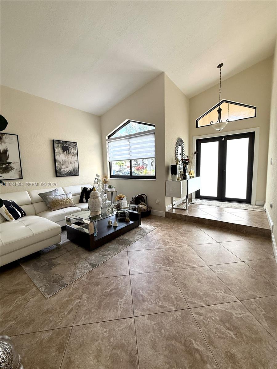 A living room features vaulted ceilings, tile flooring, a white sofa, and a glass-topped table — 8731 NW 153rd Ter, Miami Lakes FL 33018, MIAMI LAKES, FL