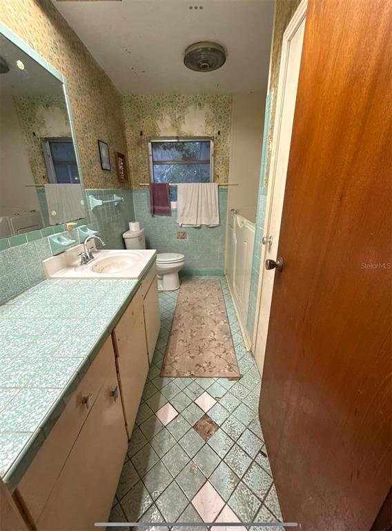 A bathroom features light blue tiled countertops and flooring, floral wallpaper, and a wooden door — 301 W LEMON STREET, BOWLING GREEN, FL