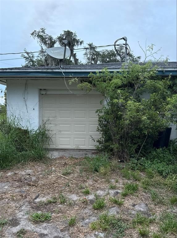 A white garage door is set into a concrete block wall with overgrown vegetation nearby — 301 W LEMON STREET, BOWLING GREEN, FL