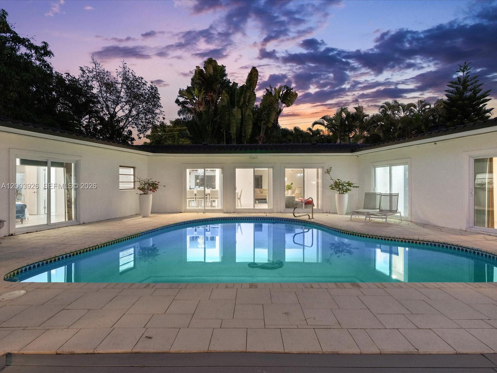 A swimming pool sits in the courtyard of a white house at sunset — 5000 Riviera Dr, Coral Gables FL 33146, CORAL GABLES, FL