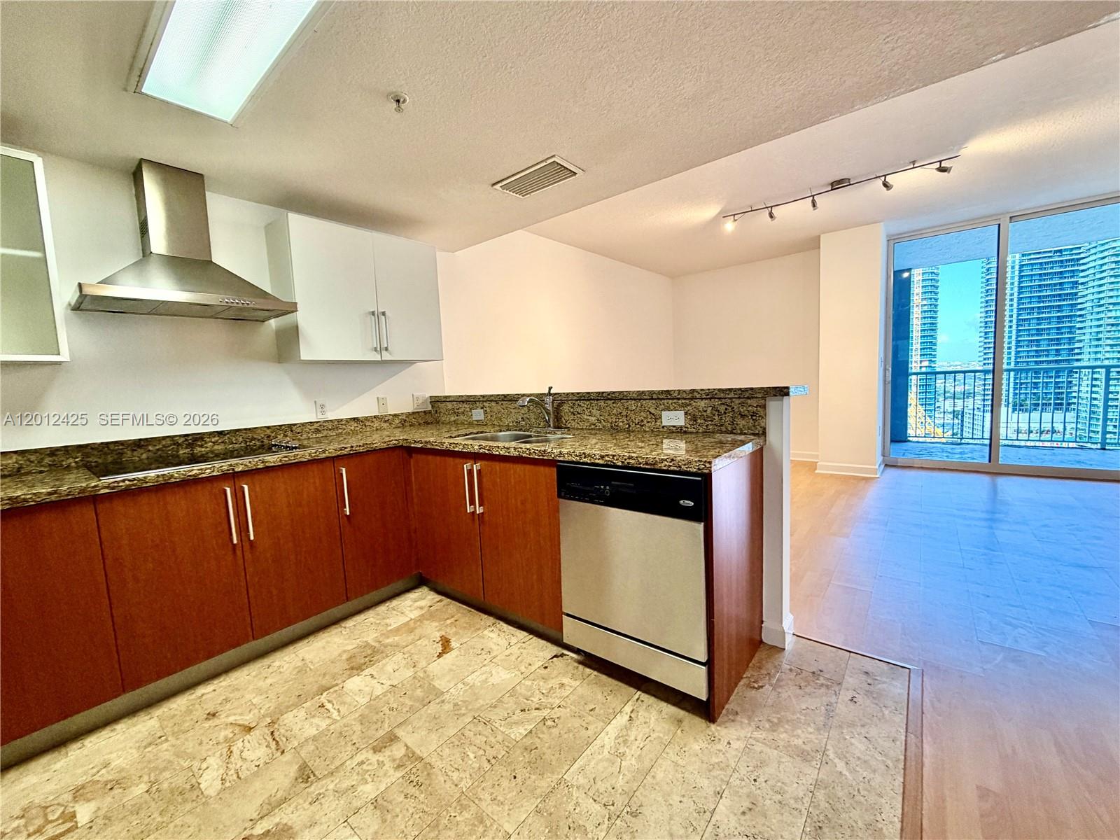 A kitchen with wood cabinets, granite countertops, and stainless steel appliances overlooks a living area — 170 SE 14th St # 2906, Miami FL 33131, MIAMI, FL