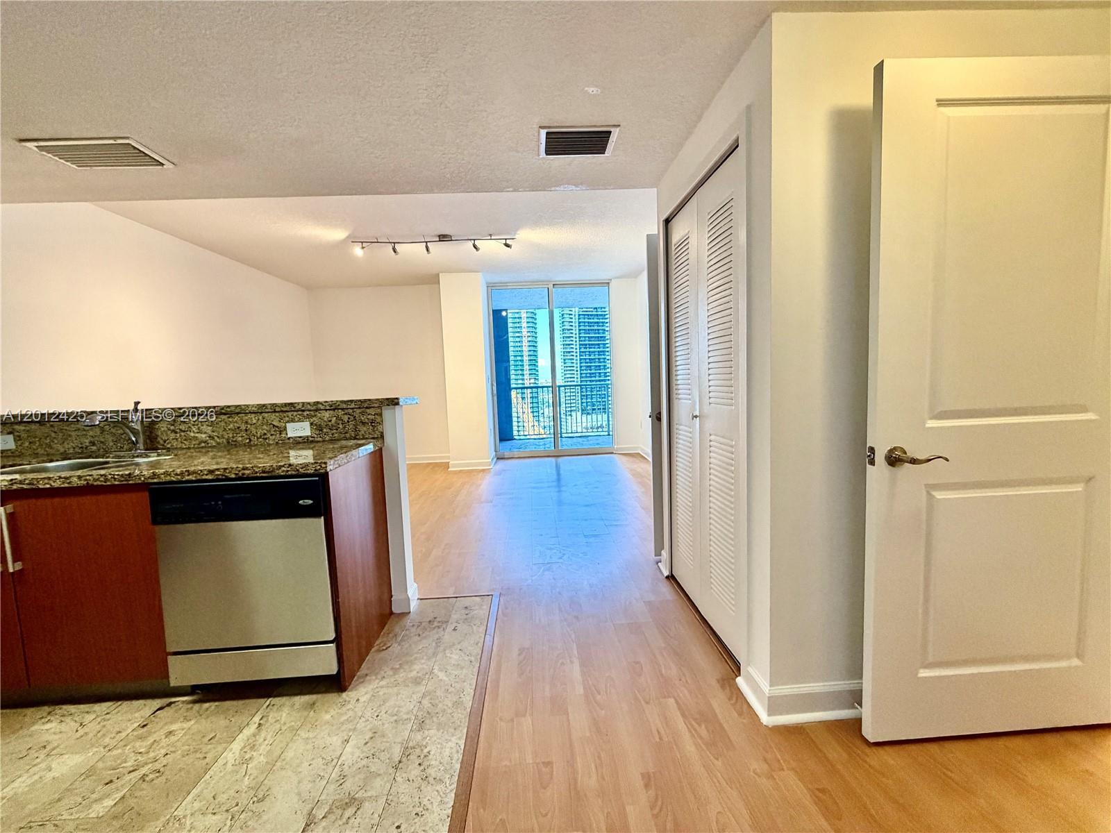 A kitchen with granite countertops and a dishwasher opens into a living area with balcony — 170 SE 14th St # 2906, Miami FL 33131, MIAMI, FL