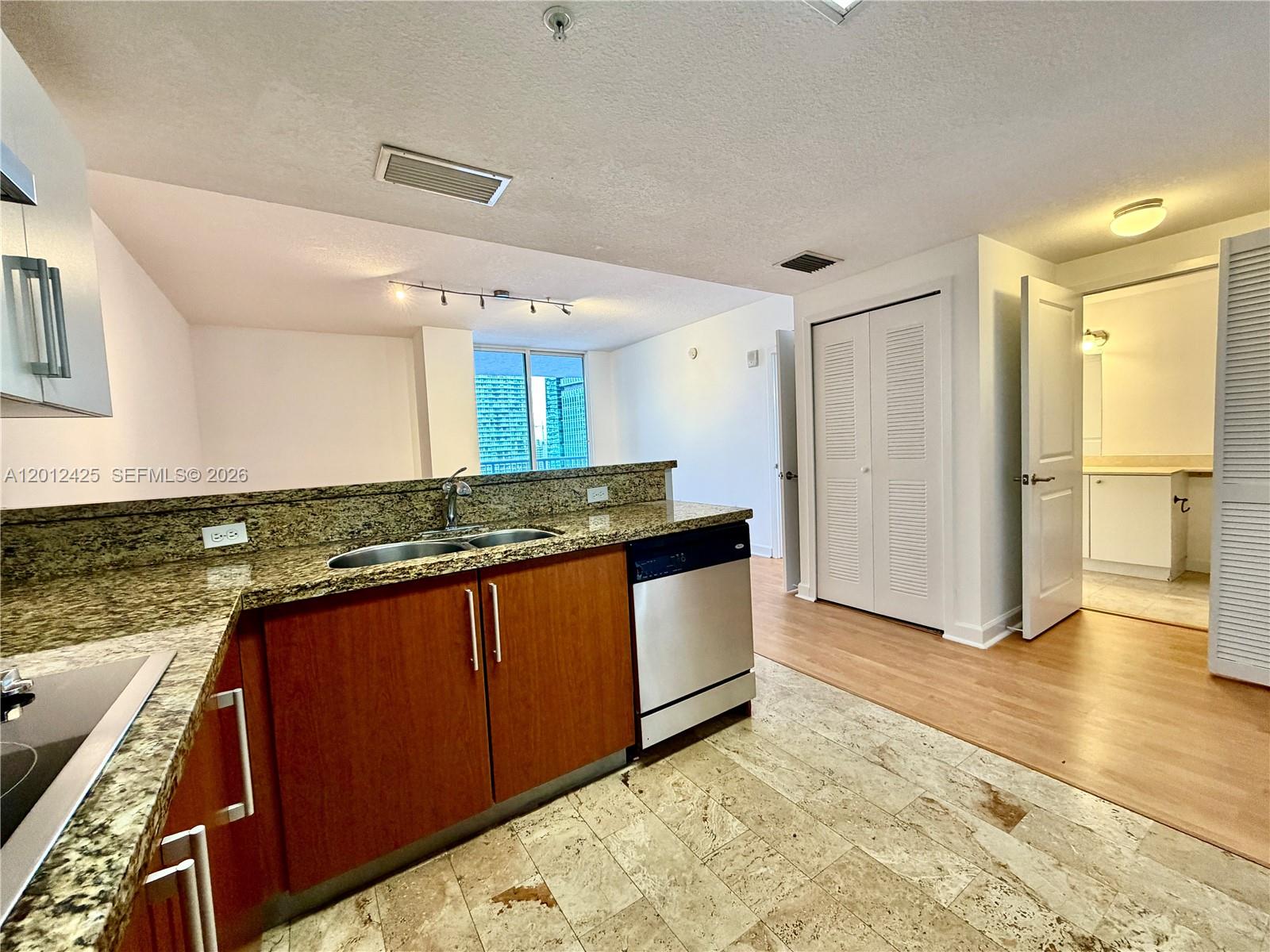 A kitchen with granite countertops, wood cabinets, and tile flooring opens to a living area — 170 SE 14th St # 2906, Miami FL 33131, MIAMI, FL