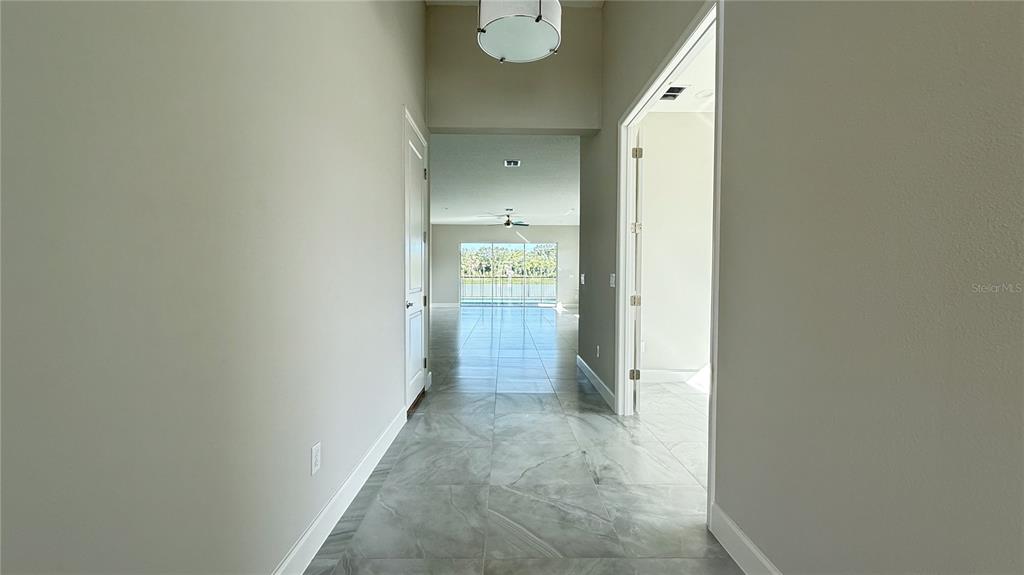 A hallway with light gray tile flooring leads toward a bright living area with water views — 32523 NEROLI STREET, WESLEY CHAPEL, FL