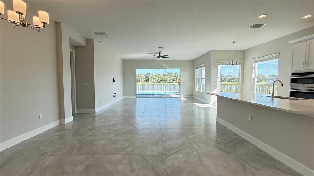 An open-concept kitchen and living area features light tile flooring and sliding glass doors — 32523 NEROLI STREET, WESLEY CHAPEL, FL