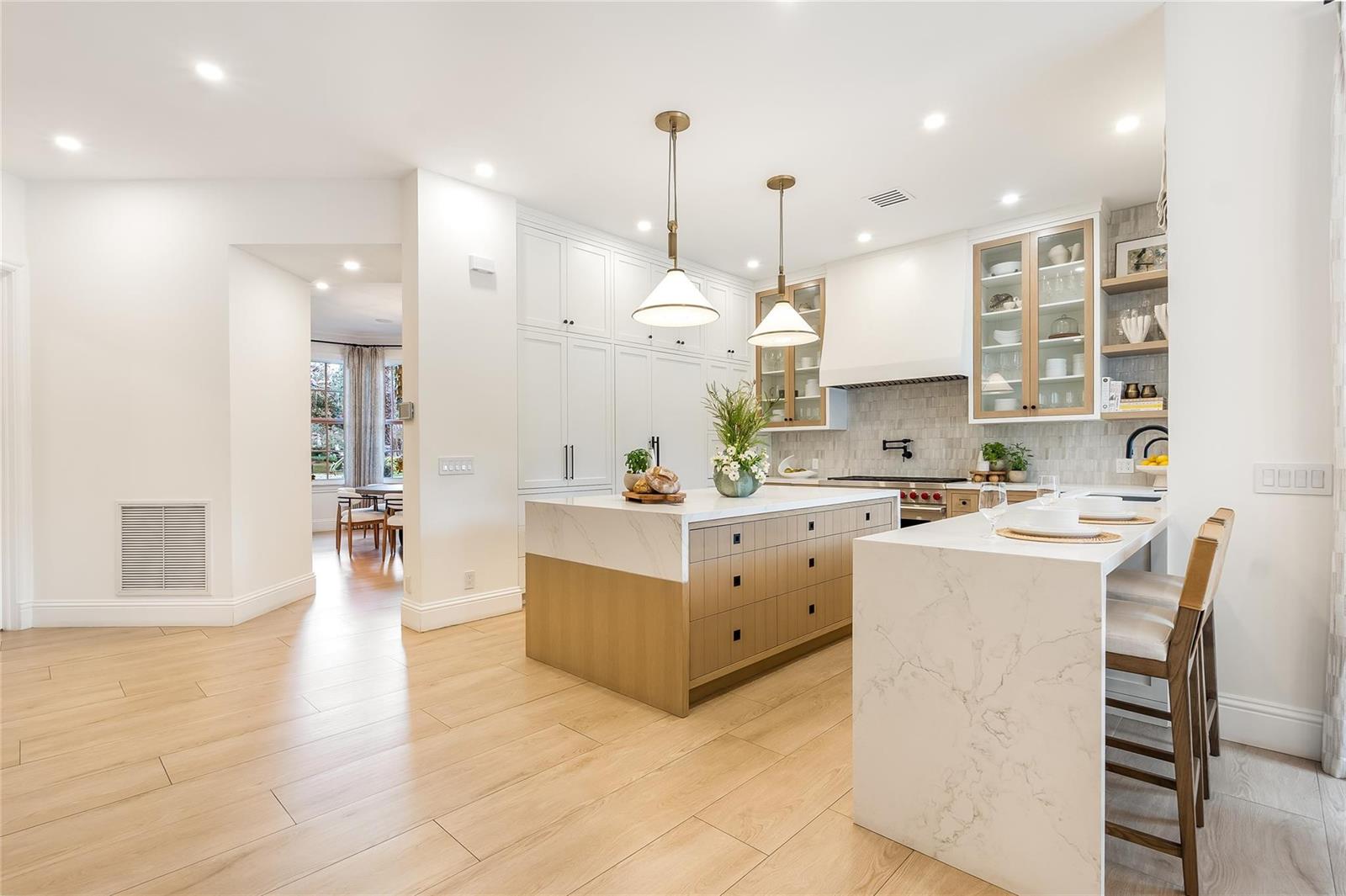 A modern kitchen features a marble-topped island, light wood cabinetry, and white pendant lights — 2825 Hackney Road, Weston FL 33331, WESTON, FL