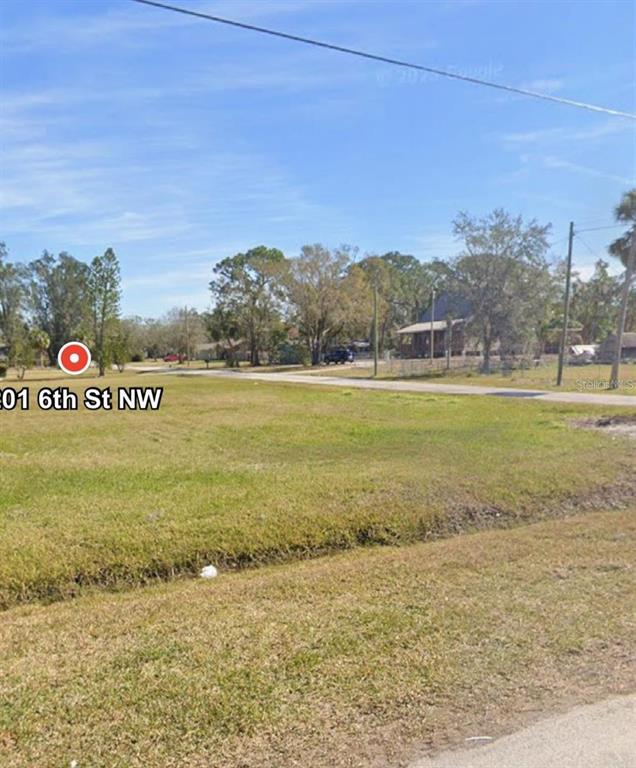 This is a street-level view of a vacant, grassy lot with trees in the background — 201 6TH STREET NW, RUSKIN, FL