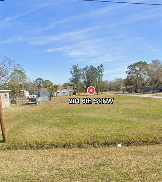 A vacant, grassy residential lot is shown under a clear blue sky — 201 6TH STREET NW, RUSKIN, FL