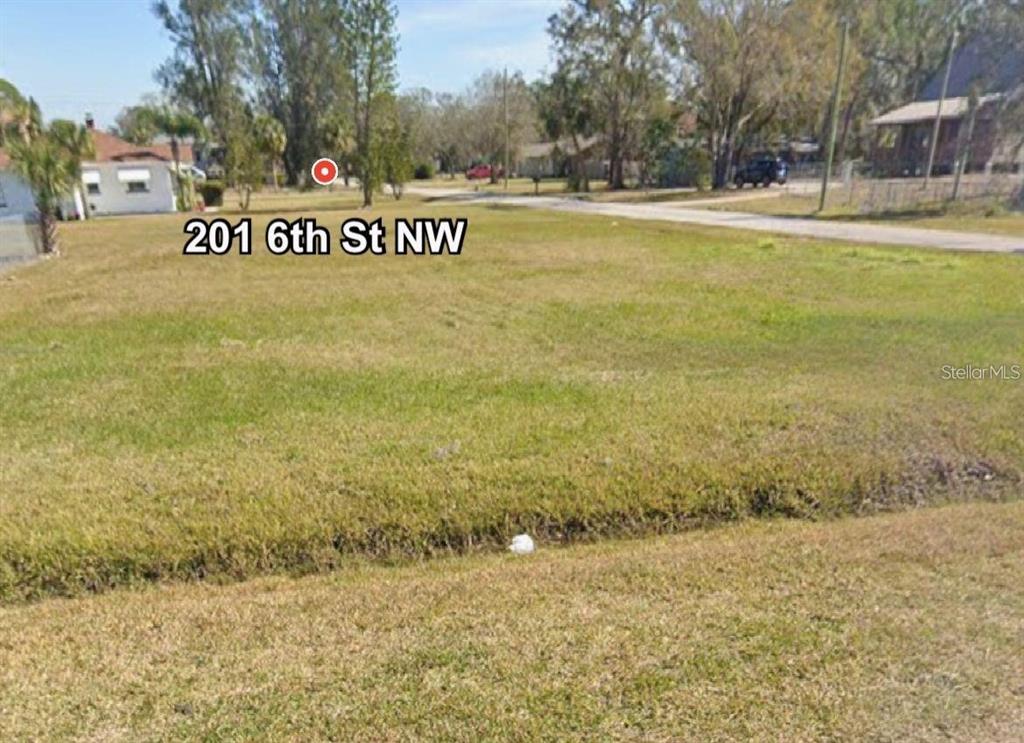 A vacant, grassy residential lot is shown from a slightly elevated street-level perspective — 201 6TH STREET NW, RUSKIN, FL