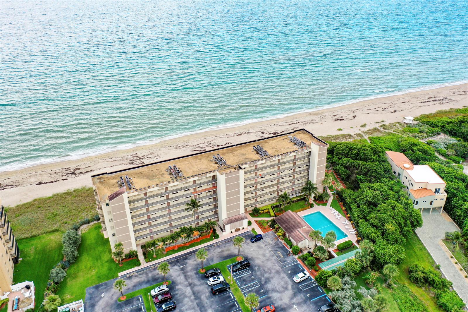 An aerial view shows a multi-story beachfront apartment building with a pool and parking lot — 10310 S Ocean Drive # 405, Jensen Beach FL 34957, JENSEN BEACH, FL